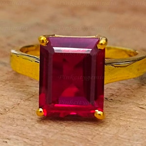 Könnte beinhalten: Ein goldener Ring mit einem großen, tief roten, smaragdgeschliffenen Edelstein.