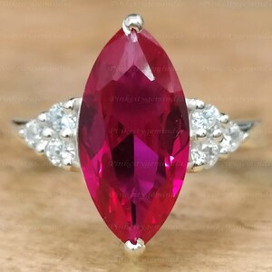 Peut inclure: Une bague en argent avec une pierre de rubis taille marquise et des petites pierres blanches sur les côtés.