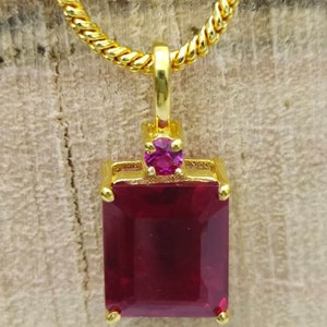 Pode incluir: Um colar de corrente de ouro com um pingente que apresenta uma gema grande, retangular, de cor vermelha escura com uma gema redonda menor de cor rosa na parte superior.