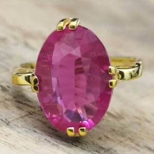 May include: A gold ring with a large oval pink gemstone. The ring has a simple design with a smooth band and a bezel setting for the gemstone.