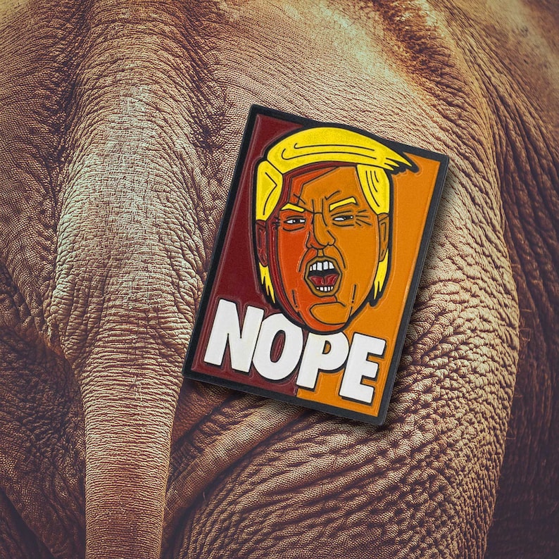 May include: A rectangular patch featuring a stylized illustration of a person with blonde hair and an orange complexion, mouth open in an expression of shouting. The word NOPE is printed in large white capital letters at the bottom of the patch.