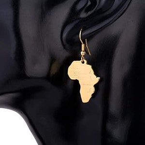 Puede incluir: Pendientes de tono dorado con un mapa de África. Los pendientes son colgantes y tienen un cierre de gancho.