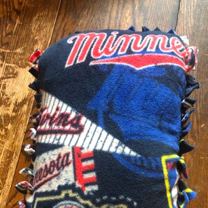 Puede incluir: Una almohada de franela azul, roja y blanca con el logotipo de los Minnesota Twins y la palabra "Minnesota" en ella.