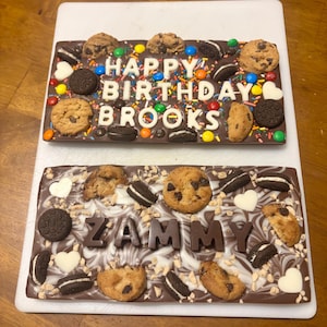 Può includere: Due barrette di cioccolato con diversi condimenti e messaggi. La barretta superiore dice "Happy Birthday Brooks" e la barretta inferiore dice "Zammy".