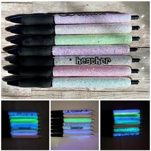 May include: A set of eight black pens with glitter-covered barrels. The barrels are decorated with different colors and names, including "Heather". The pens glow in the dark.