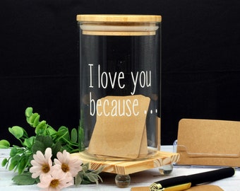 May include: A glass jar with a wooden lid and a wooden base. The jar has the text "I love you because..." written on it. The jar is filled with small brown cards.
