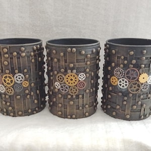 Peut inclure: Trois contenants cylindriques avec un design steampunk. Les contenants sont brun foncé avec une texture tissée et des clous métalliques. Chaque contenant est orné d'un groupe d'engrenages décoratifs de différentes couleurs métalliques, dont l'or, l'argent et le bronze.