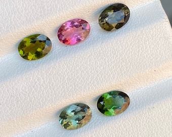 May include: Five oval-shaped gemstones on a white display card. The gemstones are green, pink, and a combination of green and brown.