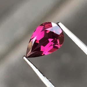 以下が含まれることがあります： ピンセットで保持された、ファセットカットされた洋梨型のピンクの宝石