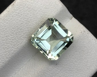 May include: A light green square-shaped gemstone with a faceted cut.