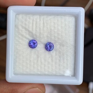 K&ouml;nnte beinhalten: Zwei runde, violette Edelsteine in einer wei&szlig;en Schachtel mit einer wei&szlig;en Baumwollf&uuml;tterung.