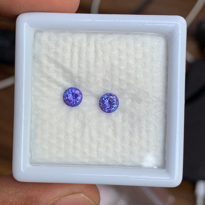 K&ouml;nnte beinhalten: Zwei runde, violette Edelsteine in einer wei&szlig;en Schachtel mit einer wei&szlig;en Baumwollf&uuml;tterung.