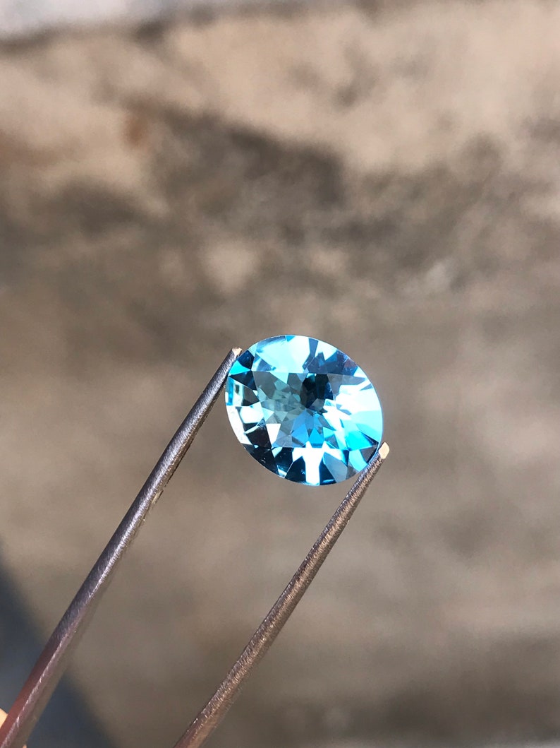 May include: A light blue oval-shaped gemstone held by tweezers against a grey background.