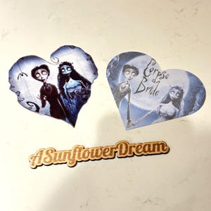 May include: Three heart-shaped decorations featuring characters from the movie "Corpse Bride." The hearts display images of the characters in shades of blue and gray. A wooden sign with the text "A Sunflower Dream" is also present.