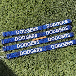 May include: Four blue straps with the word "DODGERS" in white lettering. The straps have silver metal clasps and are set against a green background. The straps are decorated with glitter.