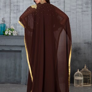 May include: A brown sheer kaftan with gold trim and embellishments. The kaftan has a long, flowing silhouette and is perfect for a special occasion.