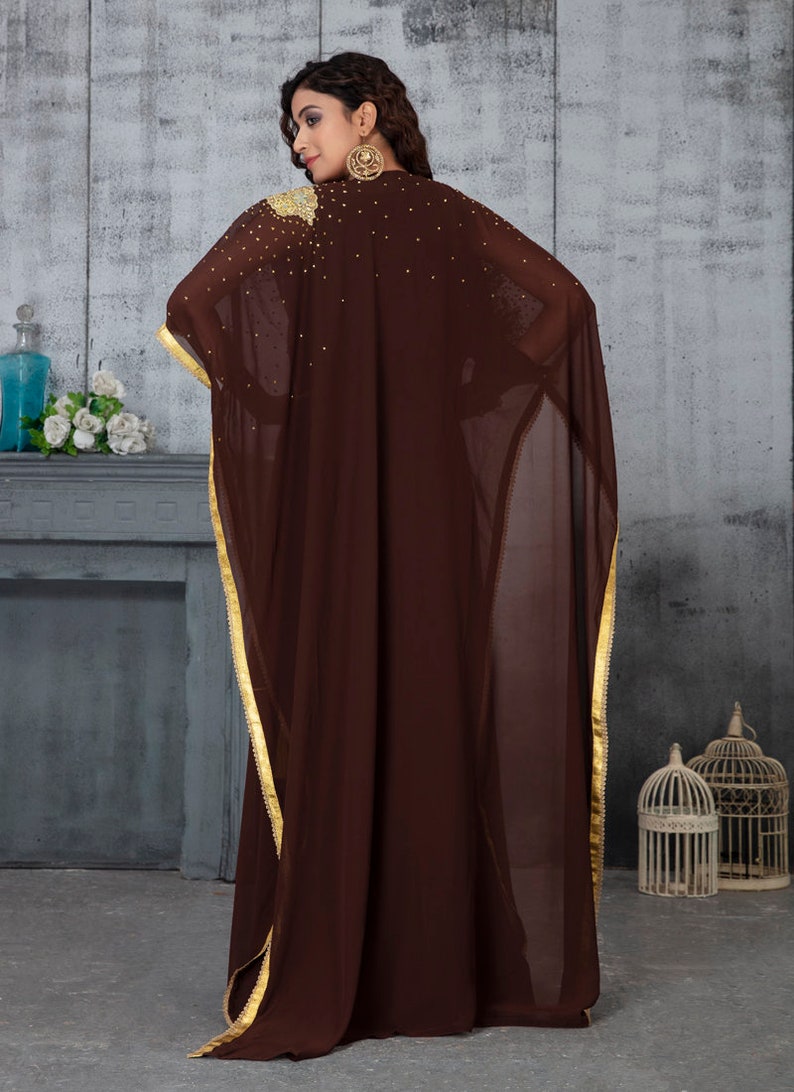 May include: A brown sheer kaftan with gold trim and embellishments. The kaftan has a long, flowing silhouette and is perfect for a special occasion.