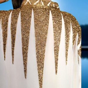 May include: A white blouse with a gold beaded design on the back. The beads are arranged in a pattern of triangles.