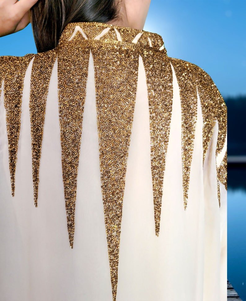 May include: A white blouse with a gold beaded design on the back. The beads are arranged in a pattern of triangles.