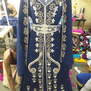 May include: A long, navy blue dress with gold and white embroidery and beading. The dress has a V-neckline and long sleeves. It is decorated with a gold belt.