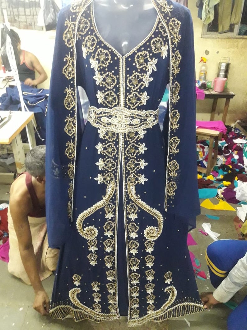 May include: A long, navy blue dress with gold and white embroidery and beading. The dress has a V-neckline and long sleeves. It is decorated with a gold belt.