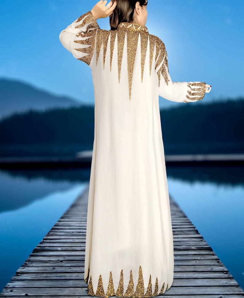 May include: A white maxi dress with a gold glitter design. The dress has a high neckline and long sleeves. The dress is decorated with a geometric pattern of gold glitter triangles.