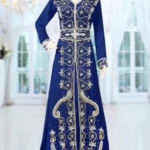 May include: A long, royal blue kaftan with gold and white embroidery. The kaftan has a V-neckline and long sleeves. It is adorned with intricate beading and sequins.