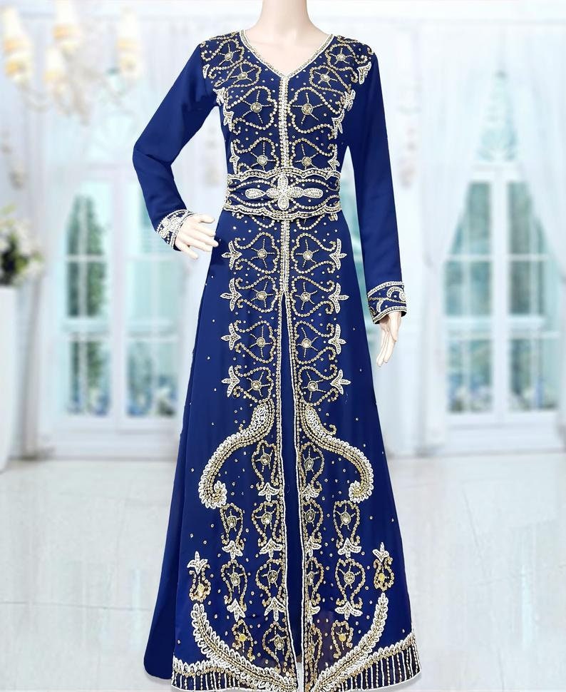 May include: A long, royal blue kaftan with gold and white embroidery. The kaftan has a V-neckline and long sleeves. It is adorned with intricate beading and sequins.