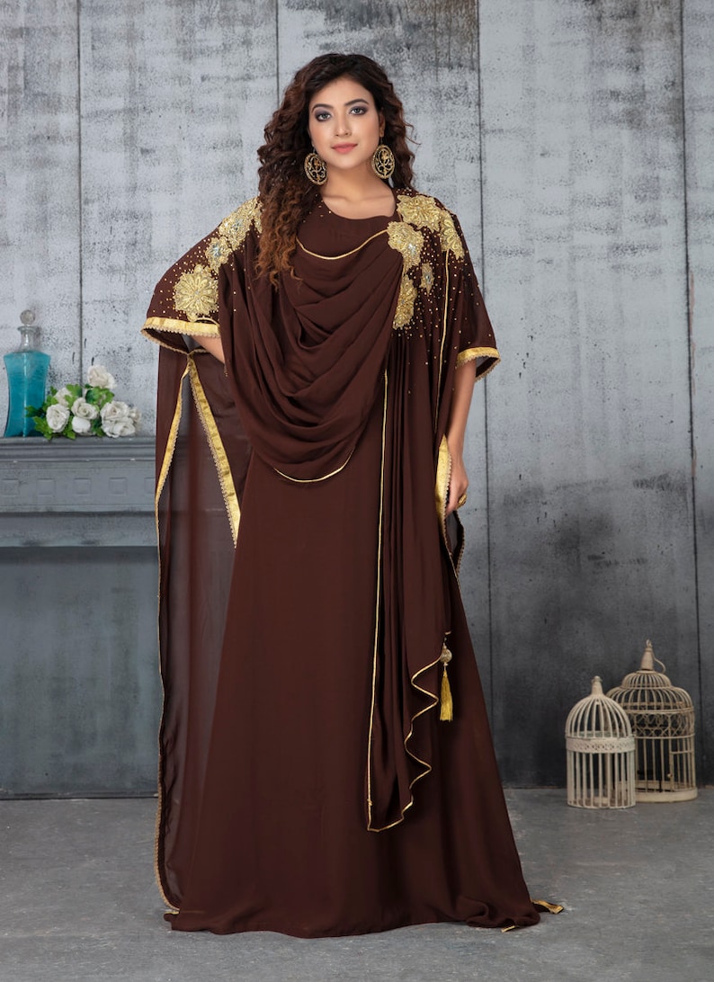 May include: A brown maxi dress with gold embroidery and a draped neckline. The dress has a long, flowing skirt and a fitted bodice. The dress is made of a soft, flowing fabric.