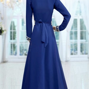 May include: A long-sleeved, royal blue maxi dress with a V-neckline and a gold embroidered design around the waist and cuffs. The dress has a tie belt at the waist.