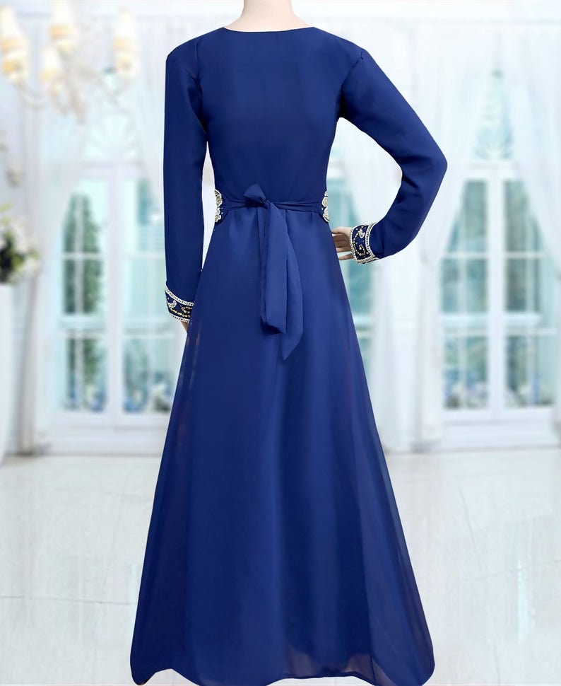 May include: A long-sleeved, royal blue maxi dress with a V-neckline and a gold embroidered design around the waist and cuffs. The dress has a tie belt at the waist.