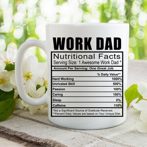 Può includere: Una tazza in ceramica bianca con una grafica nera che recita "Work Dad Nutritional Facts" con un elenco di competenze lavorative e i relativi valori percentuali. La grafica è in stile etichetta nutrizionale.