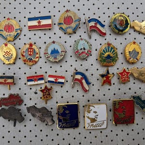 Peut inclure: Une collection de badges et d'épingles vintage avec divers motifs. Les épingles présentent des drapeaux, des étoiles et des emblèmes en rouge, bleu, or et blanc. Certaines épingles comportent du texte, d'autres des détails complexes.