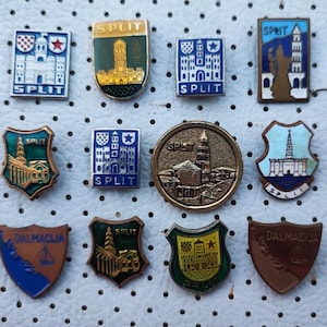 Könnte beinhalten: Eine Sammlung von zehn Vintage-Emaille-Anstecknadeln mit Motiven der Stadt Split in Kroatien. Die Nadeln sind in verschiedenen Formen und Größen und zeigen verschiedene Designs, darunter das Stadtwappen, eine Kirche und einen Turm. Die Nadeln sind alle in gutem Zustand und wären eine großartige Ergänzung für jede Sammlung.