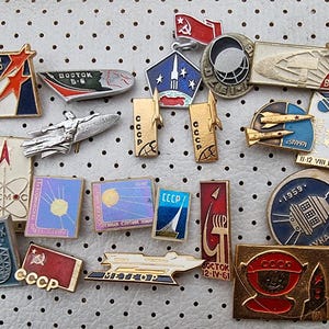 May include: A collection of vintage Soviet space programme pins. The pins feature various spacecraft, astronauts, and emblems. The pins are made of metal and have a variety of colours, including red, blue, white, and gold. The pins are in good condition and would be a great addition to any space enthusiast's collection.