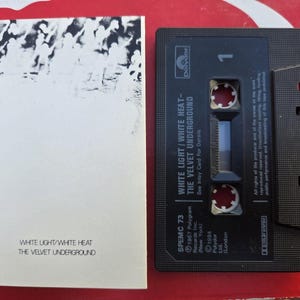 May include: A black cassette tape and a white booklet. The cassette tape has the text "WHITE LIGHT / WHITE HEAT - THE VELVET UNDERGROUND" and the number "1". The booklet has the same text.