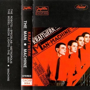 Op de afbeelding: Een vintage cassettebandje voor Kraftwerk's album "The Man-Machine". De hoes heeft een rood en zwart ontwerp met de bandnaam en albumtitel in witte letters. Vier bandleden dragen oranje shirts. De rug van de cassette toont de albumtitel en tracklijst.