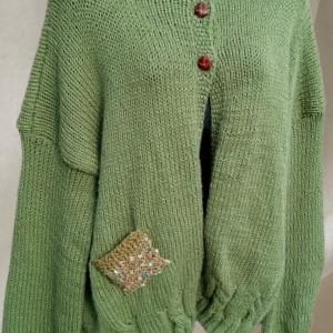 May include: A sage green knit cardigan featuring a high ribbed neckline, long sleeves with ribbed cuffs, and a ribbed hem. The front closure includes three dark brown buttons. A single square pocket with a textured, multi-coloured beaded design.