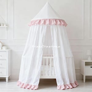 Op de afbeelding: Wit hemelbed met een conische top en vloeiende stof. De luifel heeft een roze en wit gestreepte ruchesrand. Het bed staat in een lichte, luchtige kamer met witte meubels en muren. De tekst "FriendTreeHome" is zichtbaar.