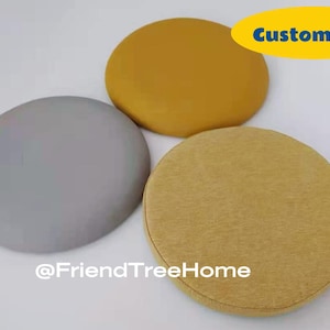 May include: Three round chair cushions in different colors. One is gray, one is yellow, and one is a darker yellow. The cushions are made of fabric and have a soft, comfortable texture. The text "Custom size" is written in blue letters on a yellow background. The text "@FriendTreeHome" is written in black letters on a white background.