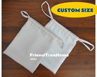 Pode incluir: Duas bolsas brancas de cordão com um cordão branco. As bolsas são feitas de um tecido macio e leve. As bolsas estão colocadas planas sobre uma superfície de madeira. O texto "FriendTreeHome 2024" está impresso nas bolsas. O texto "CUSTOM SIZE" está impresso em amarelo sobre um oval azul.