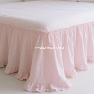 May include: A light pink bed skirt with a ruffled edge. The bed skirt is made of a soft fabric and has a gathered design. The text "FriendTreeHome" is visible on the skirt.