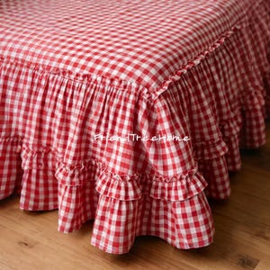 May include: A red and white gingham bed skirt with a ruffled edge. The fabric is a classic check pattern, creating a country or farmhouse aesthetic. The text "FriendTreeHome" is visible on the fabric.
