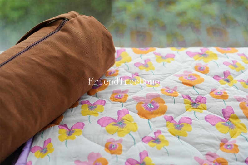 May include: A brown canvas yoga mat bag with a zipper closure, resting on a white and floral patterned fabric with the text "FriendTreeHome".