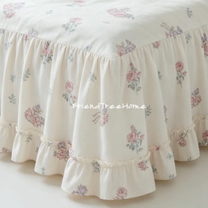 Può includere: Gonna da letto color crema con un motivo floreale di rose rosa e grigie. La gonna ha un bordo a balze, creando un'estetica delicata e romantica. Il tessuto sembra essere cotone o un materiale simile.