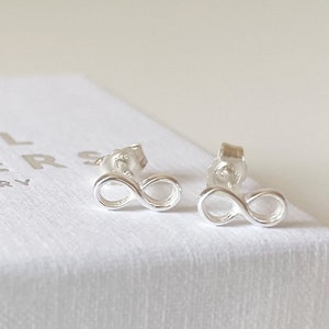 May include: A pair of silver infinity symbol earrings in a white box with the text "Shell Seeker Jewellery".