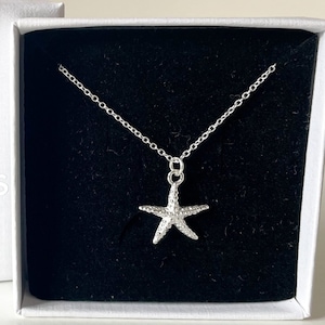 May include: A silver starfish necklace in a white box with the text "SHELL SEEKERS JEWELLERY" on the lid.