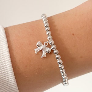 Puede incluir: Una pulsera de plata con cuentas y un dije de lazo.