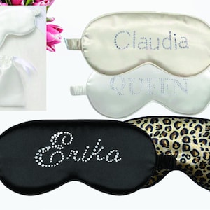Peut inclure: Trois masques de sommeil en satin avec des noms brodés en strass. Les masques sont blancs, noirs et à imprimé léopard. Les noms sont Claudia, Queen et Erika.