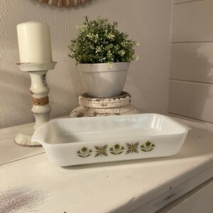 May include: White rectangular baking dish with a green and yellow floral pattern. The dish is on a white wooden surface.